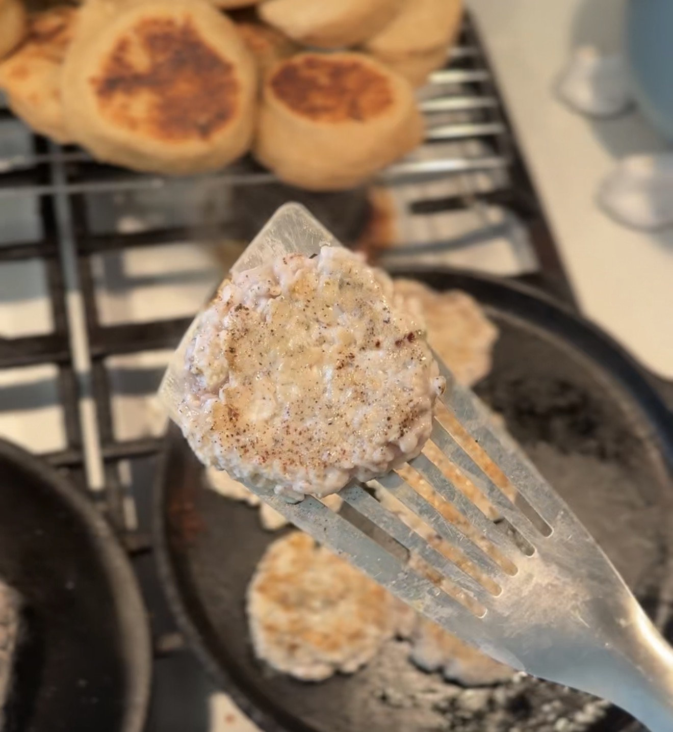 Homemade maple and sage chicken sausage patty on a spatula over a cast iron skillet
